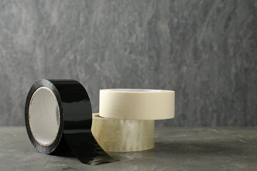 Rolls of different adhesive tapes on grey table, space for text