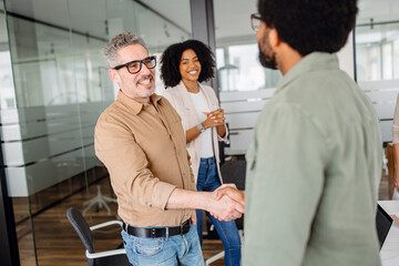 Fototapeta premium A professional handshake between two business colleagues in a modern office. Smiling coworkers observe, symbolizing agreement, teamwork, and successful partnership in a collaborative work environment.