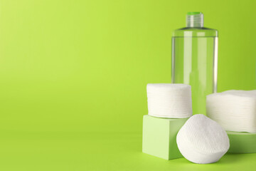Clean cotton pads and micellar water on green background. Space for text