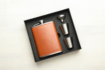 Fototapeta premium Hip flask, cups and funnel in package on light wooden table, top view