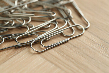 Many metal paper clips on wooden table, closeup. Space for text