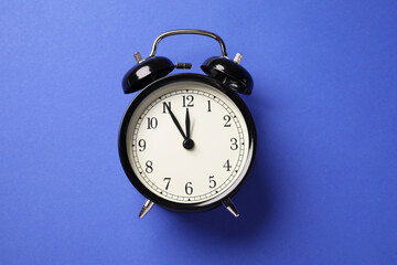 One black alarm clock on blue background, top view