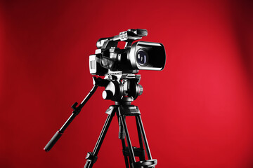 Modern video camera with tripod on red background, space for text