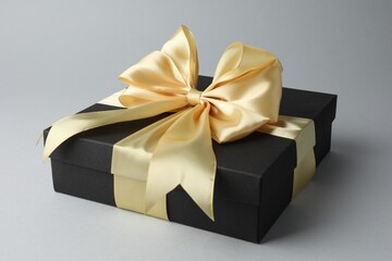 Gift box with golden bow on grey background, closeup