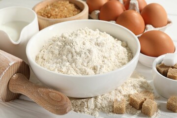 Rolling pin and ingredients for dough on white wooden table, closeup