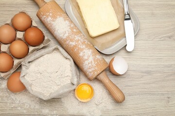 Rolling pin and different ingredients on light wooden table, flat lay