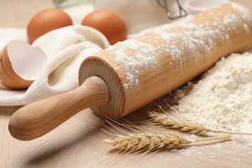 Rolling pin, flour and eggs on wooden table, closeup
