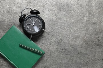 Time for knowledge. Alarm clock, notebook and pen on grey textured table, flat lay. Space for text