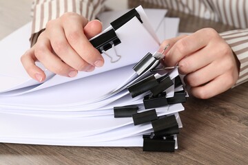 Woman holding sheets of paper with metal binder clips at wooden table, closeup