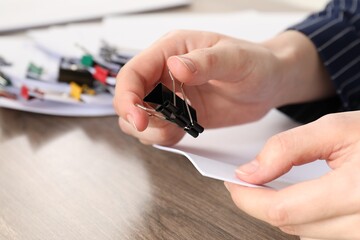 Woman attaching sheets of paper with metal binder clip at table, closeup