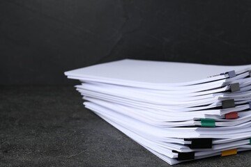 Colorful binder clips with sheets of paper on dark textured table, closeup. Space for text