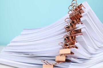 Binder clips with sheets of paper on light blue background, closeup