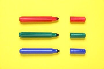 Many colorful markers on yellow background, flat lay