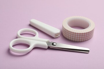 Scissors and decorative craft tape on violet background, closeup