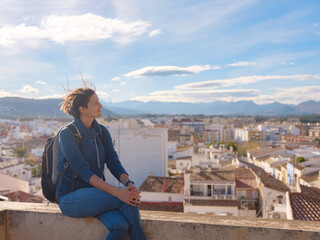 Young woman exploring historic castle in Denia, Alicante province, Spain, scenic views of town below, set against cooler season backdrop. blend of history and tranquility in timeless setting.