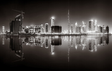 Urban city skyline with illuminated skyscrapers and waterfront railing in black and white at night, Dubai Marina bay UAE