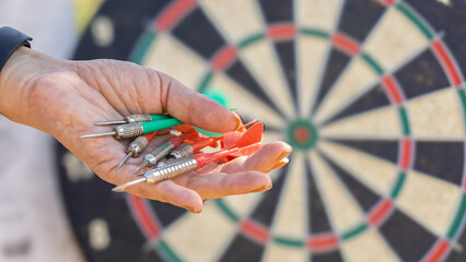Hand holding red and green darts with dartboard in background, ready for a game.