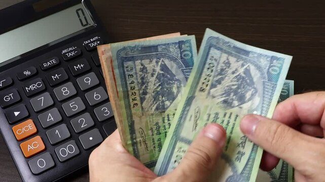Closeup view of man's hands counting Nepalese rupee (NPR) cash money banknotes. Concept of saving money for retirement, cash settlement, financial success, literacy and income planning in Nepal.