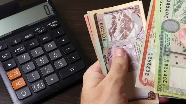 Closeup view of man's hands counting Nepalese rupee (NPR) cash money banknotes. Concept of saving money for retirement, cash settlement, financial success, literacy and income planning in Nepal.