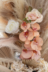 Close-up of an elegant artificial flower arrangement featuring soft beige pampas grass, dried palm leaves, and realistic faux flowers, including blush pink orchids, cream roses, and ivory hydrangeas