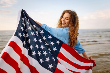 Happy woman with an American flag having fun on the seashore. Young tourist feeling free and...