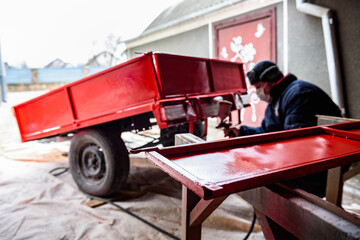 Rebuilding upgrading and modifying trailer. Man painting a metal trailer with spray gun.