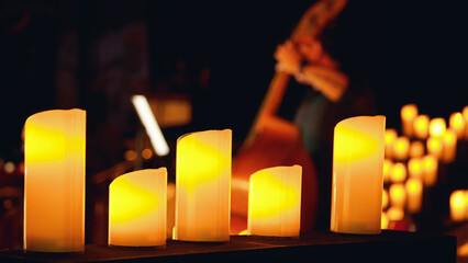 A close-up of a row of lit candles in the foreground with a blurred background of a double bass player. Candlelight concert.