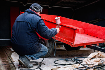 Rebuilding upgrading and modifying trailer. Man painting a metal trailer with spray gun.