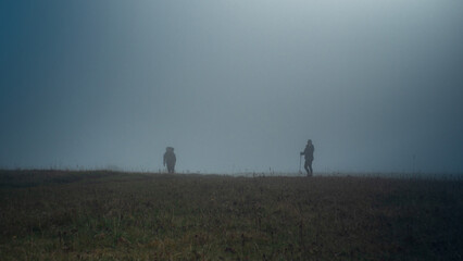 Two silhouettes of tourists with backpacks in a misty field. Mountain hiking. The atmosphere is...
