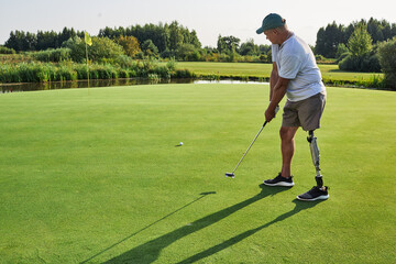 A passionate golfer uses a prosthetic leg to swing a putter on a lush green course under clear skies