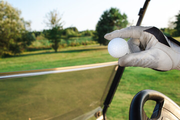 A golfer holds a white ball in hand, ready to take a shot while positioned beside a golf cart on a...