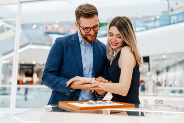 Beautiful couple enjoying in holiday shopping at modern jewelry store. Men fashion and consumerism concept.