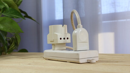 Cavi elettrici collegati alla ciabatta con spina schuko su sfondo neutro con foglie verdi.