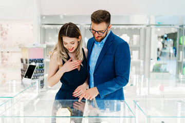 Obraz premium Beautiful couple enjoying in shopping at modern jewelry store. Young woman try it out gorgeous and expensive necklace and earrings. Fashion style and consumerism concept.
