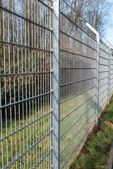 Metal wire mesh fence protecting an industrial area with trees in background