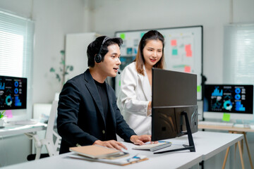 Two Asian businesspeople discussing marketing data on computer screen, working together in office