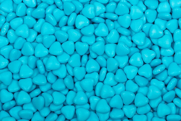 Close-up of blue heart-shaped candy with a glossy surface, forming a seamless background. Sweet confectionery texture perfect for Valentine's Day, love, and romance themes.