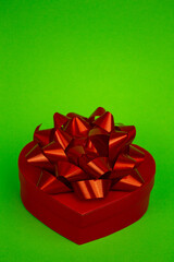 A red heart-shaped box with a red bow close-up. Gift Box on Green Background