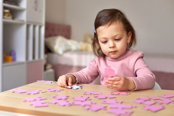 Fototapeta premium Cute little child girl assembling pink puzzle pieces on wooden desk in room