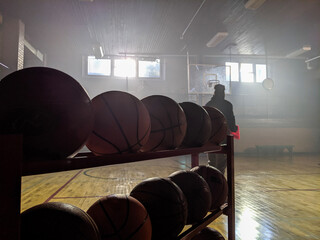 A quiet gymnasium setting lit by soft natural light, featuring basketball equipment and a shadowy figure in the distance, evoking themes of sports, solitude, and inspiration.