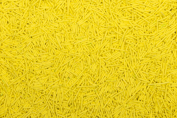 Close-up of uncooked yellow vermicelli pasta, small cylindrical noodles scattered in a textured background. Detailed food texture ideal for culinary, packaging, and ingredient concepts.