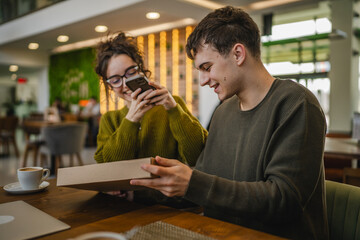 man and woman scan package card box together via mobile phone at cafe