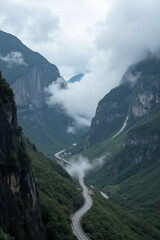 A winding road through a lush green valley surrounded by towering mountains, with clouds hanging low in the sky