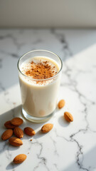 Glass of creamy white liquid with sprinkled nut on marble surface.