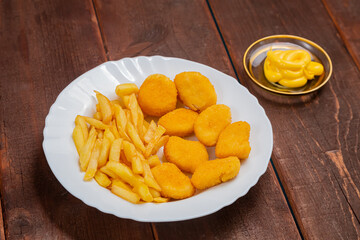 French fries and golden chicken nuggets in a plate next to cheese sauce