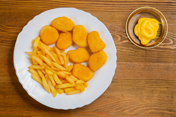French fries and golden nuggets with cheese sauce on a small wooden table