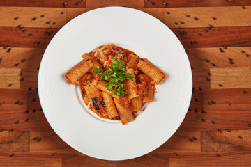 Tomato sauce chicken rigatoni topped with parmesan cheese and fresh parsley, beautifully served on a white plate for an elegant dining experience.