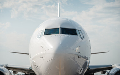 Close-up view of front part of white airplane in the ground. Symmetric view of aircraft nose, cloudy sky in the background.