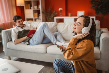 happy woman with headphones listen music ad sing while man read a book