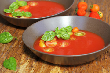 Gazpacho soup with slices of tomato, cucumber  with basil  leaves, shot from above on a dark rustic table